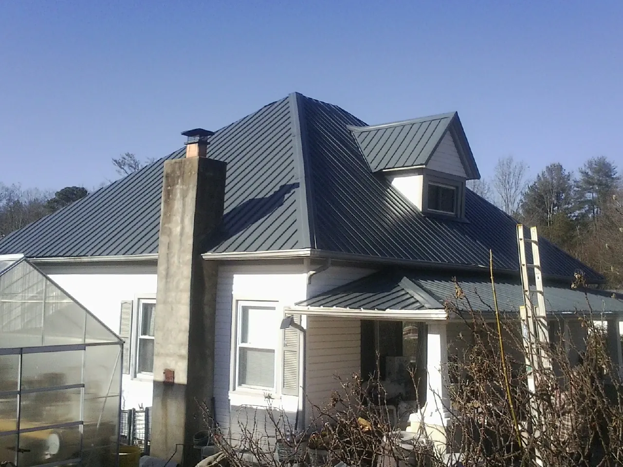 Dark blue standing seam metal roof on a white farmhouse with dormer — Slate & Tile Roof Repair by Roofing Brothers in Saltillo