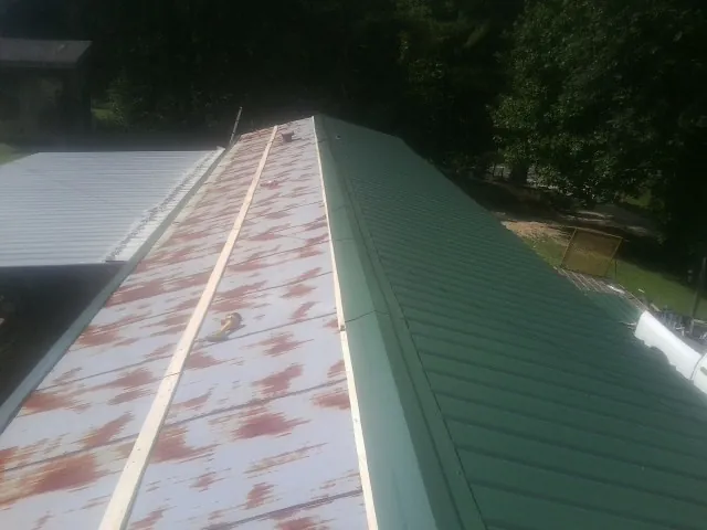 Old rusted panels beside newly installed green metal roofing — Wind Damage Roof Repair by Roofing Brothers in Saltillo