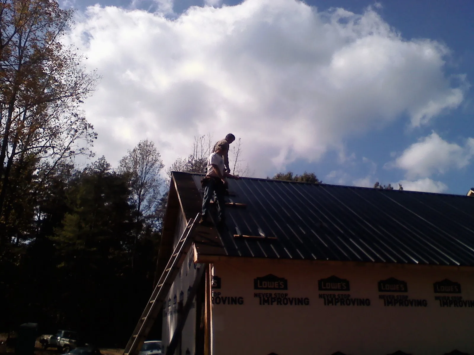 Roofer fastening dark metal panels high against a cloudy sky, from a Roof Inspection job in Saltillo